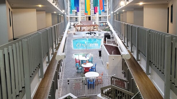 A modern hotel interior with a central pool area, multiple balconies, and a view of the pool from various angles.
