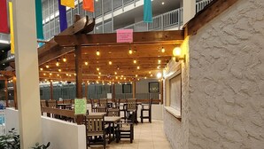 A spacious indoor area with multiple tables and chairs, a staircase, and a balcony with railings.