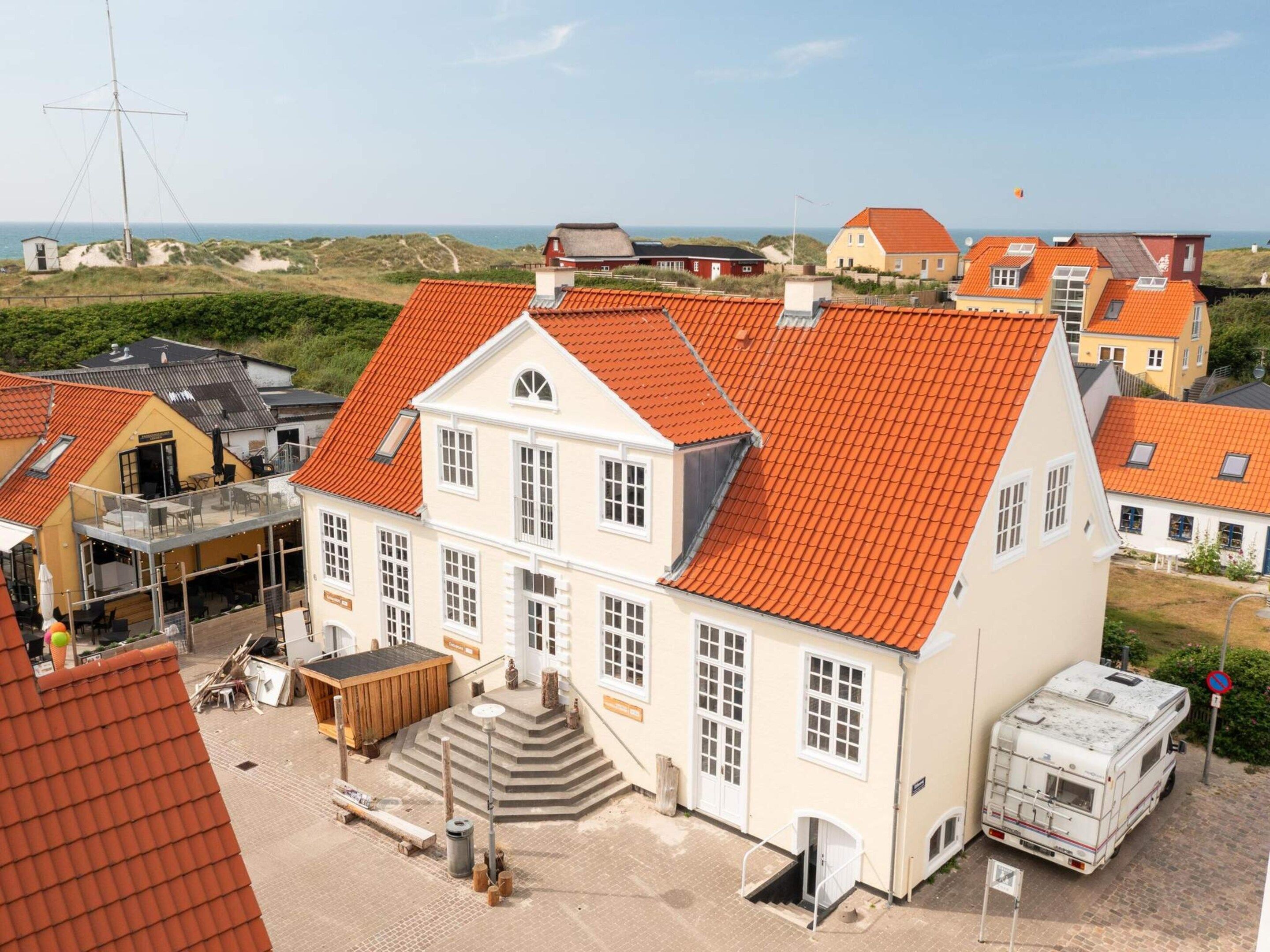 Un grand bâtiment avec un toit recouvert de tuiles rouges, un balcon et un véhicule garé à l’extérieur.
