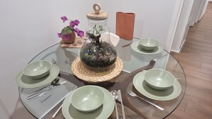 A round glass table with a woven placemat, surrounded by green plates, silverware, and a glass jar with a plant. - Beautiful lakeside unit, walk to train station, schools and Eastland (Ringwood East)