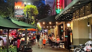 Escena de calle animada con mesas al aire libre en un restaurante llamado 'Tacos & Tequila Bar'.