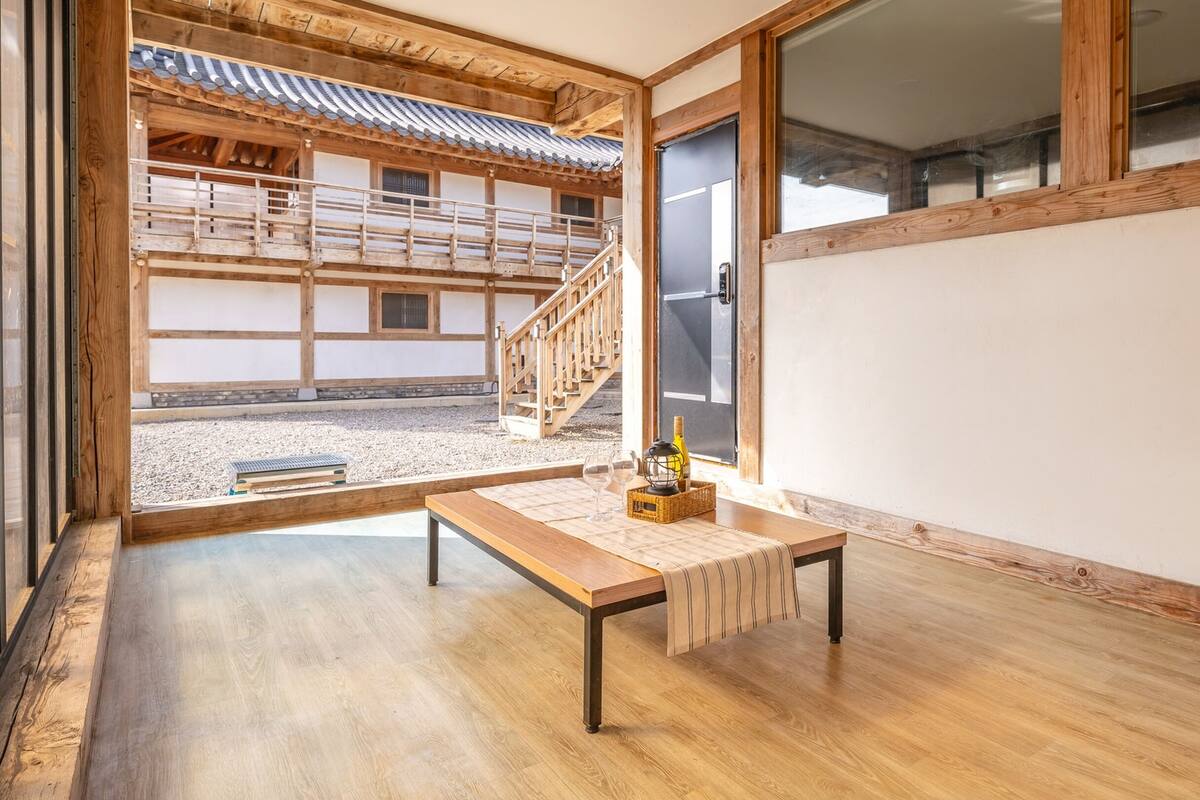 Ein traditioneller japanischer Raum mit Tatami-Böden, einem niedrigen Holztisch und Blick auf ein Holzgebäude mit Ziegeldach.