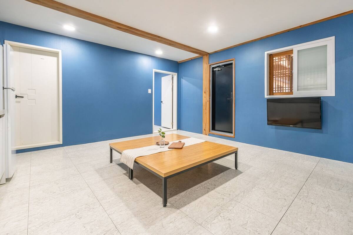 Ein Zimmer mit blauer Wand, einer Holzbank, einem Fernseher und einer Tür.