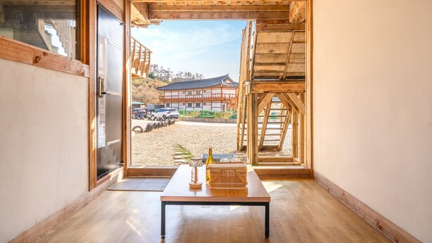 A wooden interior with a table and chairs, a view of a traditional building outside, and a gravel driveway. - Gyeongju Aratteul Hanok Pet Pension (Gyeongju)