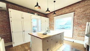Una cocina con una isla central, armarios blancos y una pared de ladrillo.