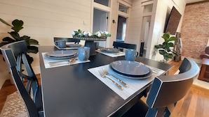 Un comedor con una mesa negra dispuesta para cuatro, incluyendo platos, cubiertos y vasos azules.