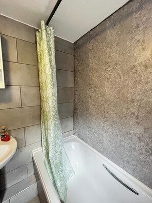 Ein Badezimmer mit einer Badewanne, einer Duschvorhang, einem Waschbecken und einem Spiegel.
