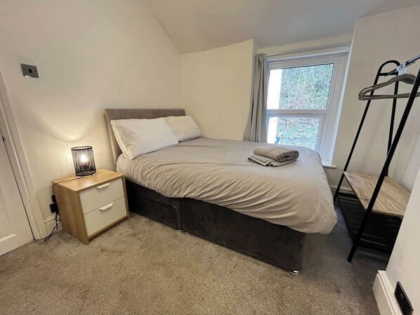 Ein Schlafzimmer mit Bett, Nachttisch, Lampe und Fenster.