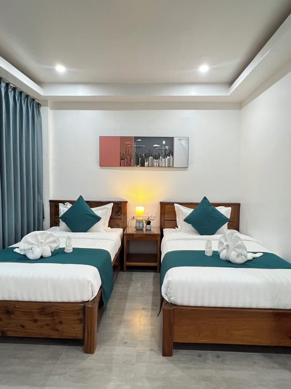 A hotel room with two wooden beds, teal bedding, and a nightstand with a lamp.