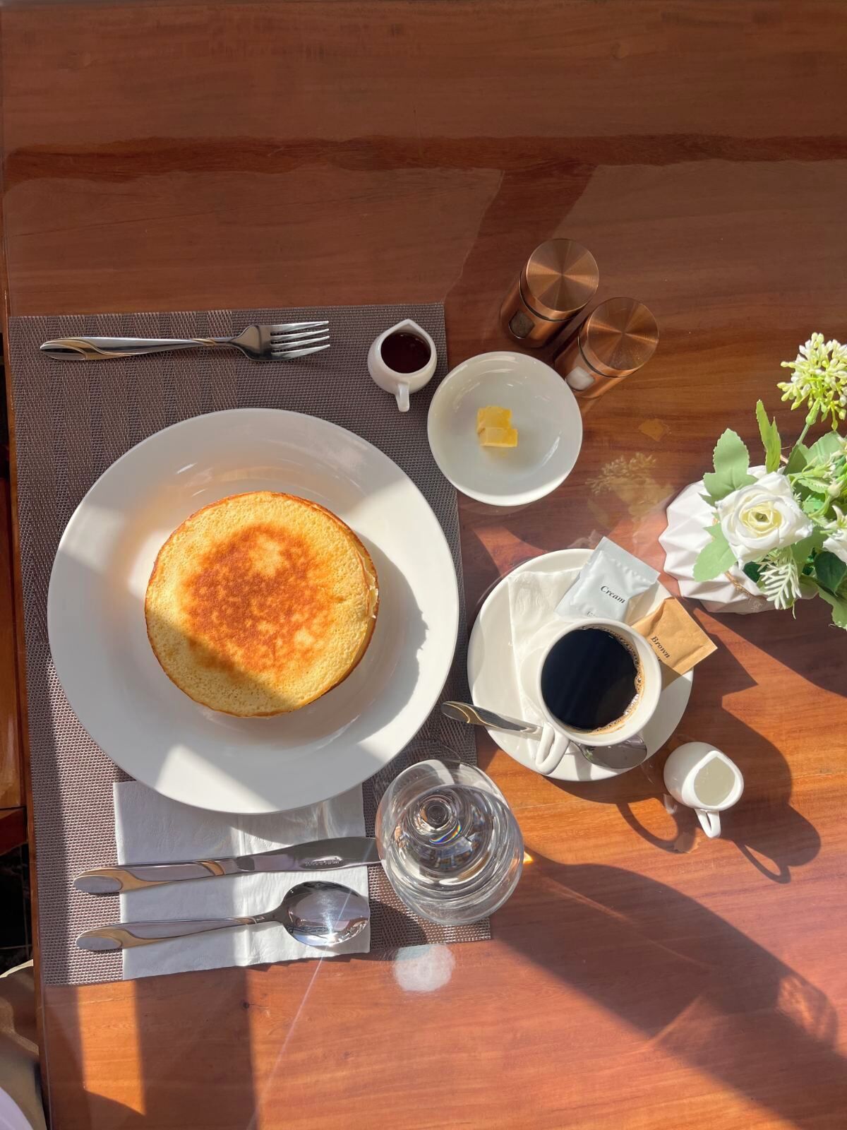 Mesa de madeira com um prato de panquecas, café, um copo de água e um pires pequeno de geleia.