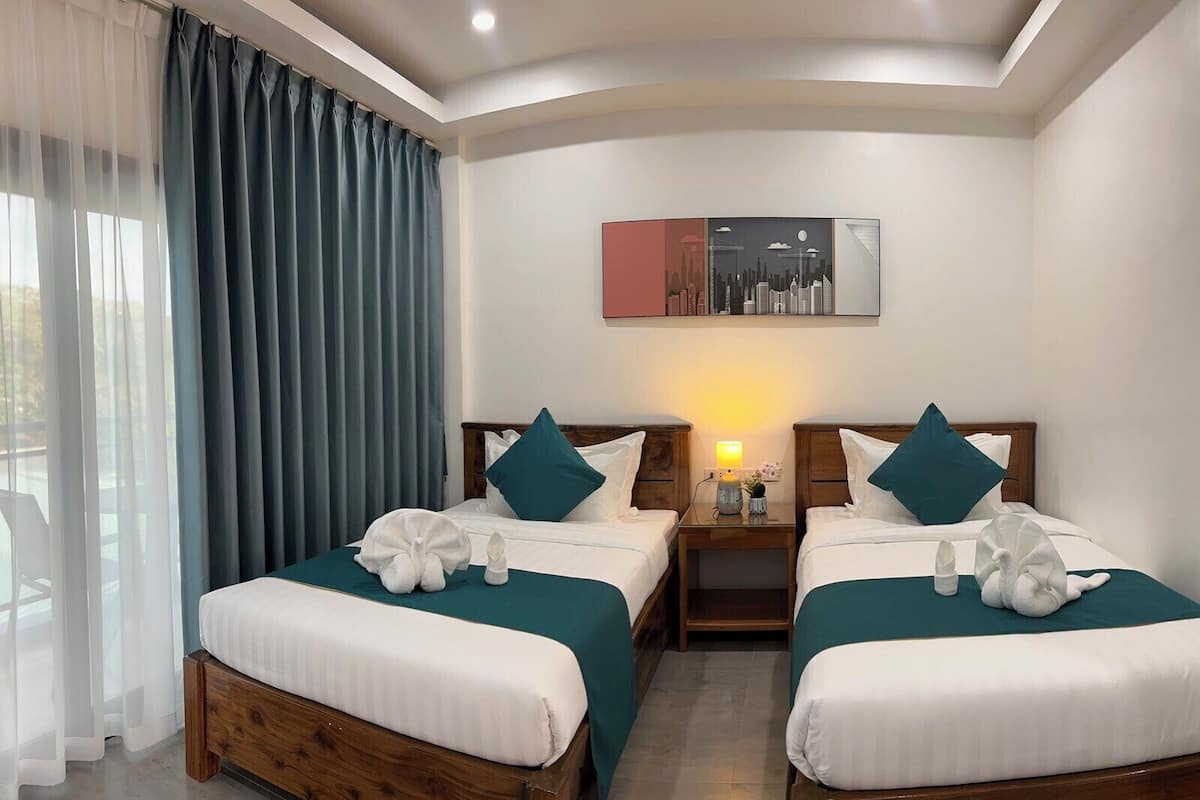 A hotel room with two beds, a nightstand, a lamp, and a painting on the wall.