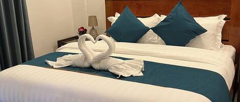 A neatly made bed with a wooden headboard, a painting of a sunset over water on the wall, and a pair of slippers on the floor.