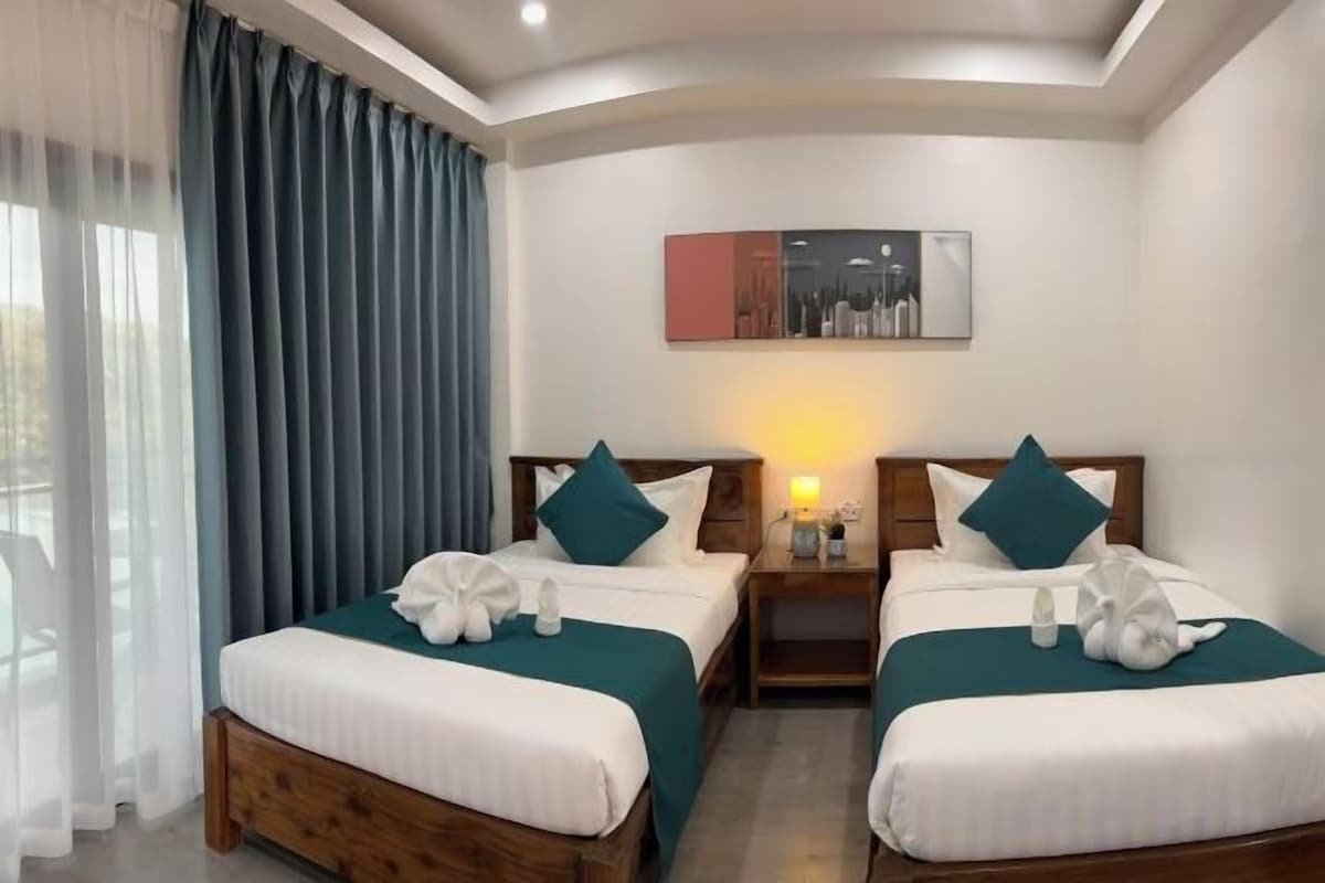 A hotel room with two beds, a nightstand, a lamp, and a painting on the wall.