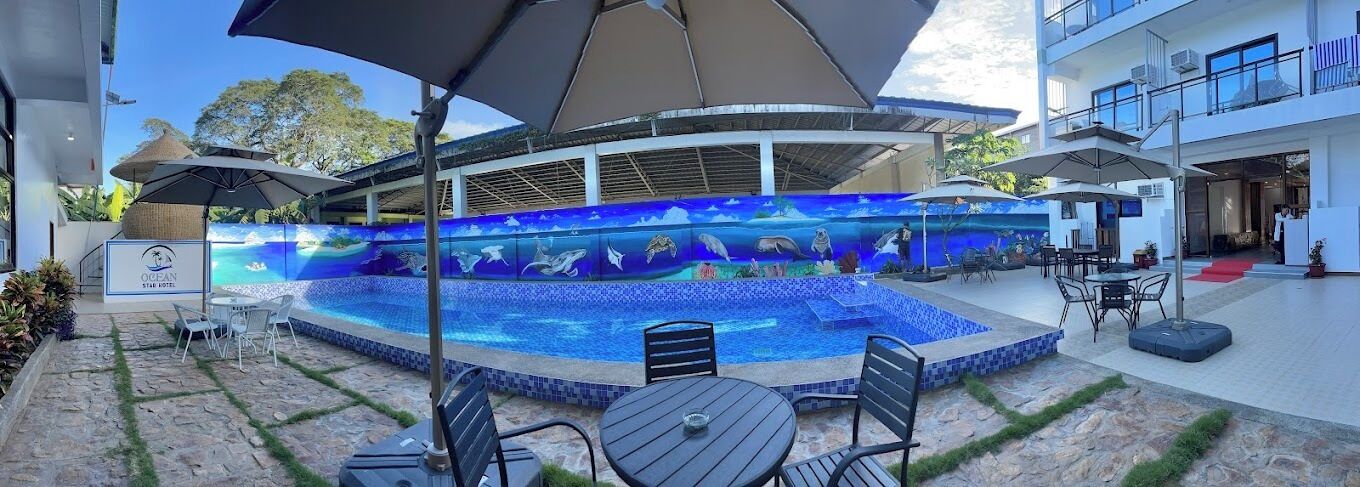 An outdoor pool area with a blue mosaic wall, seating, and umbrellas.