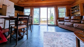 A wooden interior with a dining area, a sofa, and a view through large glass doors.