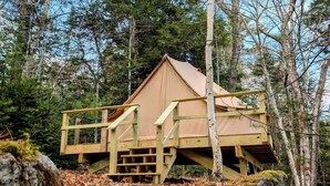 A cabin with a wooden deck and stairs, surrounded by trees.
