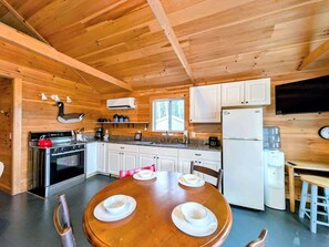 Interior de una cabaña de madera con cocina, mesa de comedor y sillas.