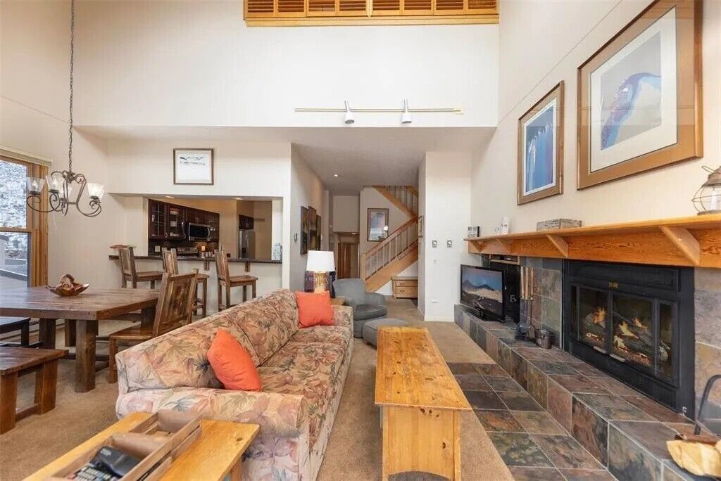 A spacious living room with a fireplace, a dining area, and a kitchen in the background.