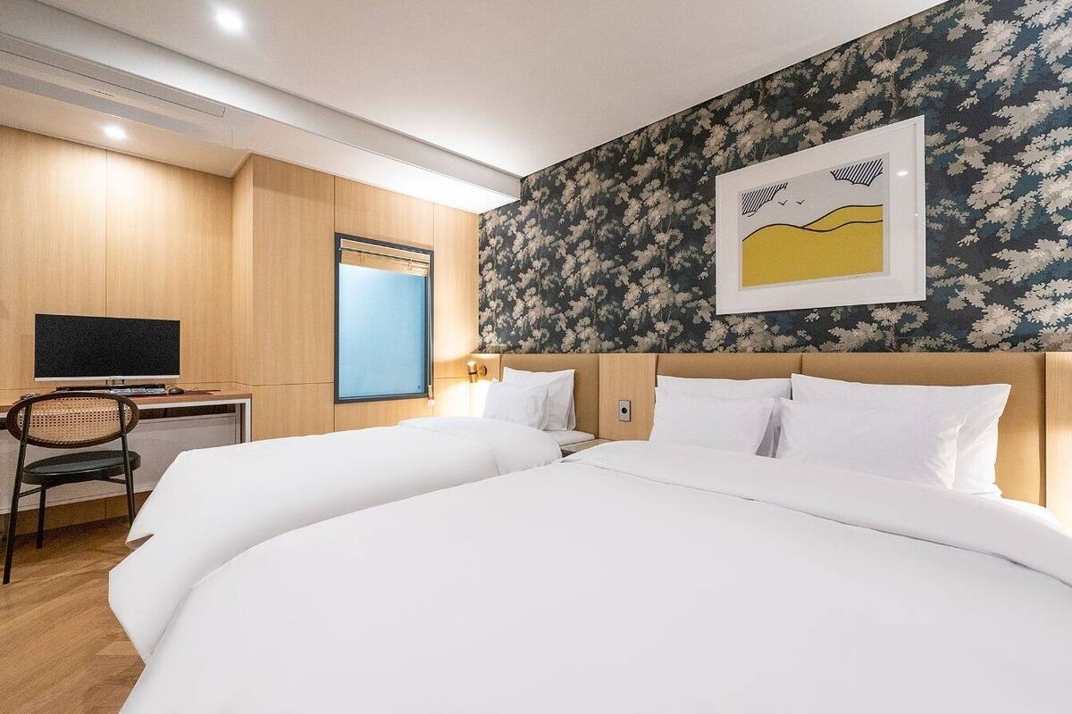 Une chambre d’hôtel avec deux lits, un bureau avec un ordinateur et une grande fenêtre.