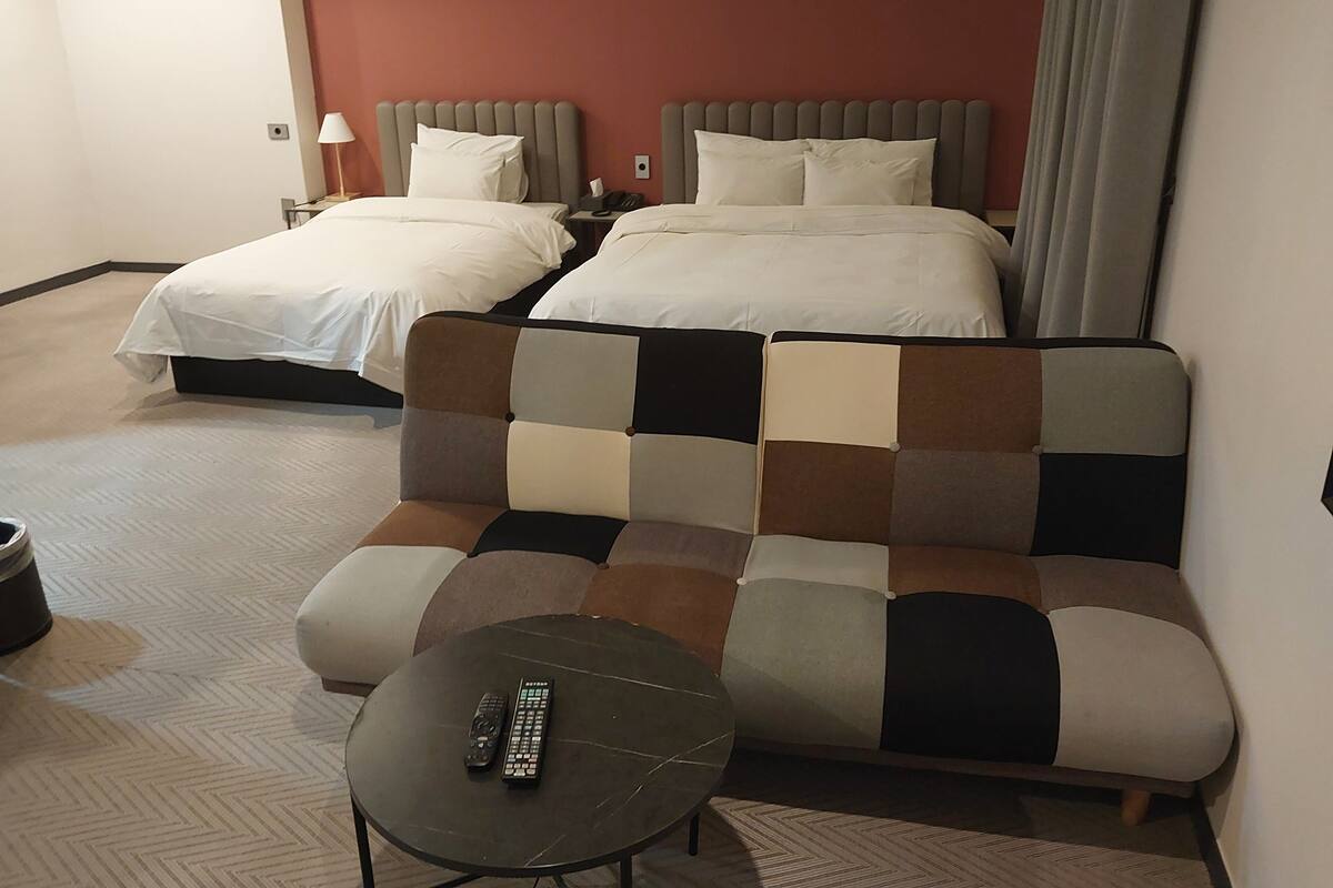 Une chambre d’hôtel avec deux lits, un canapé, une petite table et une télécommande posée sur la table.