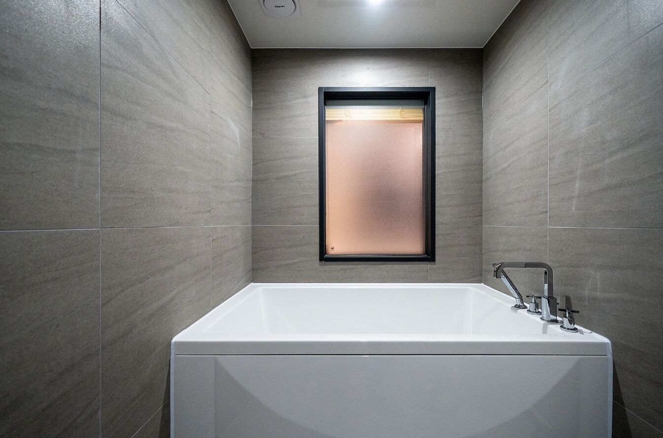 Un baño moderno con una bañera grande, un espejo instalado en la pared y un ventanal pequeño.