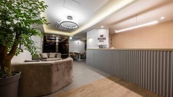 A modern hotel lobby with a reception desk, seating area, and a large tree.