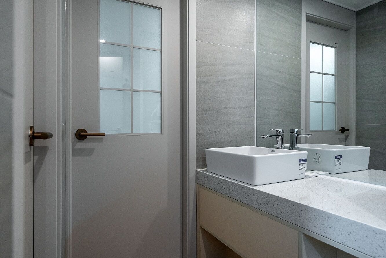 A modern bathroom with a double sink, frosted glass door, and a large mirror.