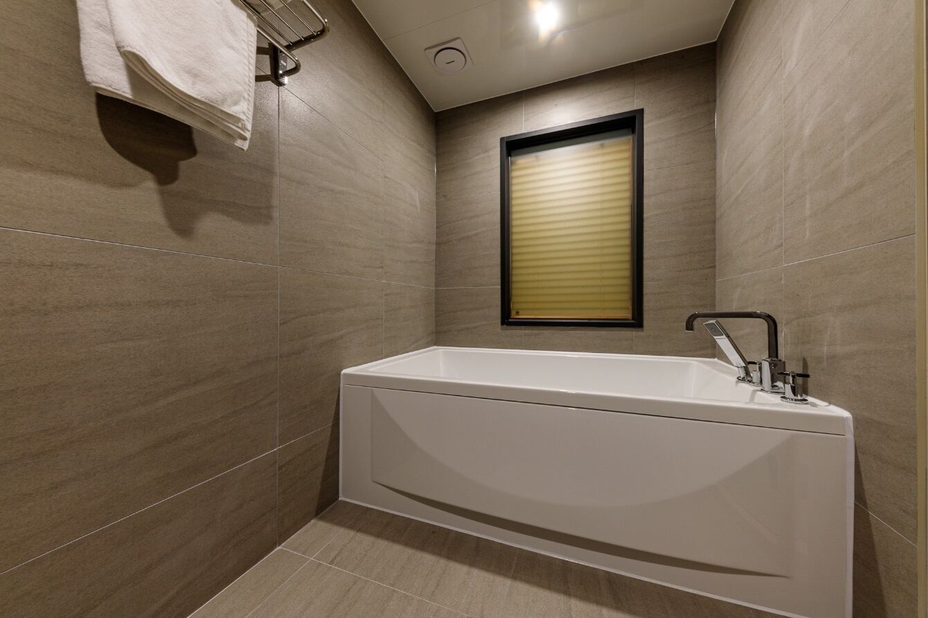 A modern bathroom with a freestanding bathtub, a towel rack, and a window with blinds.