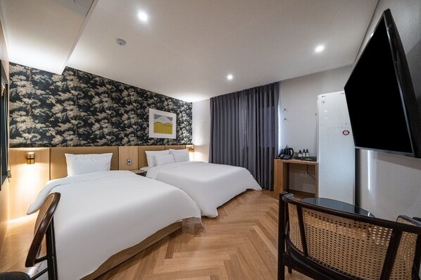 A hotel room with two beds, a flat-screen TV, a small table, and a chair.