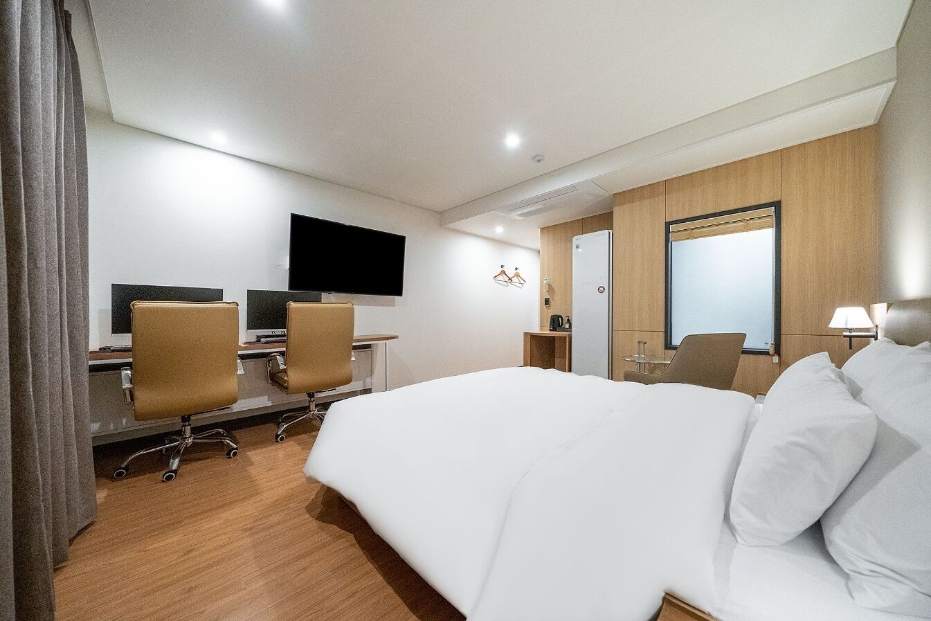 A hotel room with a large bed, a desk with two chairs, a flat-screen TV, and a wooden wardrobe.