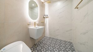 Une salle de bain avec un lavabo blanc, un miroir, une douche dotée d’un robinet doré et des carreaux de sol à motifs.