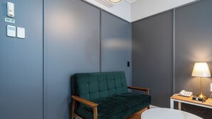 Une pièce avec un canapé vert, une table blanche avec une lampe et un téléphone.