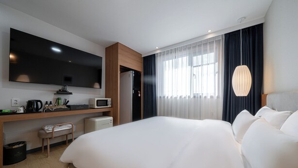 Une chambre d’hôtel avec un lit, un bureau doté d’un micro-ondes, une télévision et une fenêtre avec des rideaux.