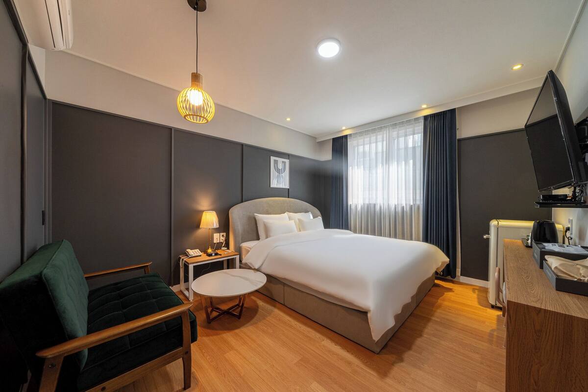 Een moderne hotelkamer met een bed, bureau, stoel, rond tafel, lamp, televisie en plafondlamp.