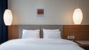 Une chambre d’hôtel avec un grand lit, deux tables de chevet, une tête de lit en bois et deux lampes suspendues.