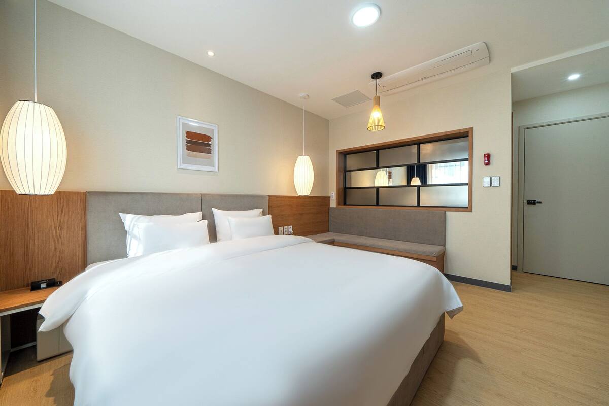 Hotelkamer met groot bed, nachtkastjes, bureau, stoel, wandplank en deur.