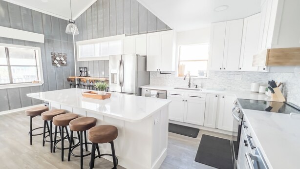 A modern kitchen with white cabinetry, a large island with stools, a built-in oven, and a dining area with a bar stool.