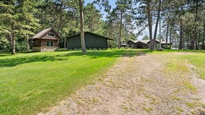 A cabin with a stone foundation, surrounded by a grassy area and tall trees.
