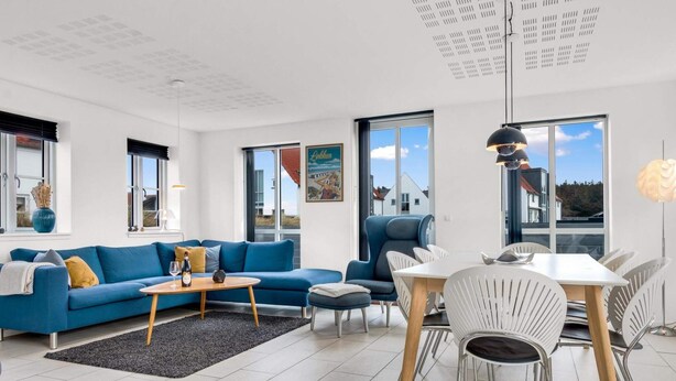 Ein modernes Wohnzimmer mit einem blauen Sofa, einem Esstisch mit Stühlen und großen Fenstern.