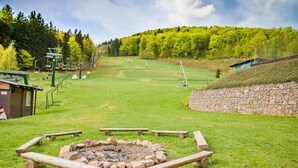 Ein Rasenbereich mit Feuerschale, Picknicktischen und einem Sessellift im Hintergrund.