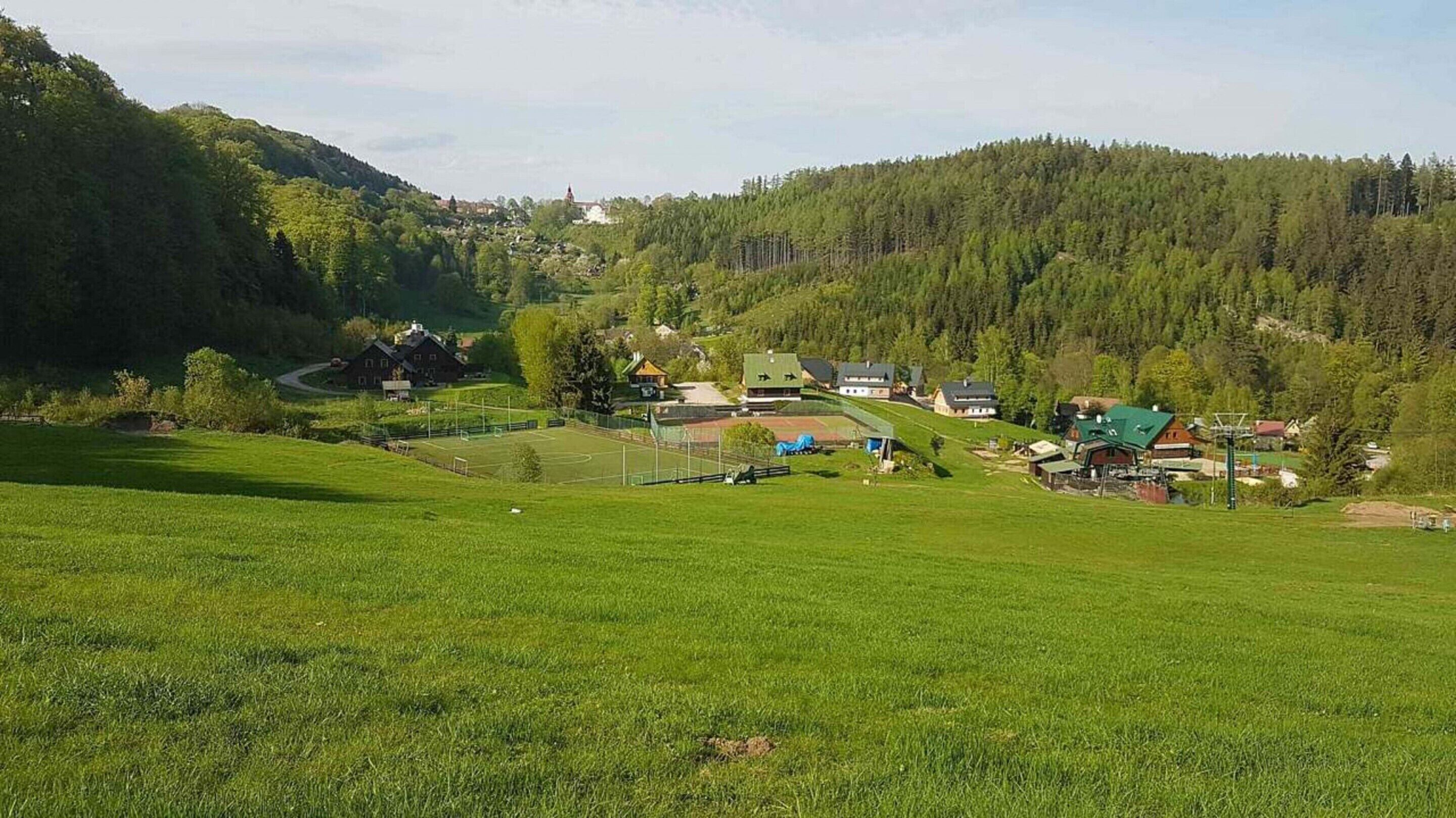 A rural landscape with a green field, a small building, and a forested hill in the background.