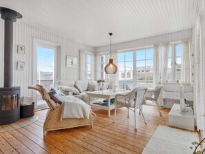 A cozy room with a fireplace, wicker furniture, and large windows. - 5 Star Holiday Home in Lokken (Lokken)