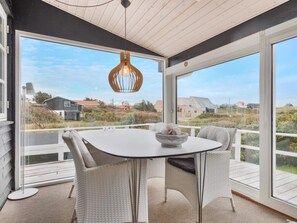 A covered outdoor seating area with a table and chairs, a hanging light fixture, and a view of houses in the distance. - 5 Star Holiday Home in Lokken (Lokken)