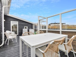 Une terrasse extérieure avec une table blanche et des chaises en osier, donnant sur une pelouse.