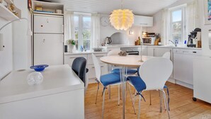 A modern kitchen with white cabinetry, a round dining table, and blue chairs. - 5 Star Holiday Home in Lokken (Lokken)