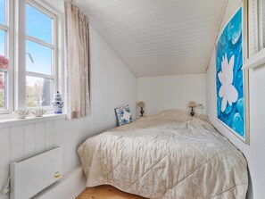A bedroom with a bed, a radiator, a window with curtains, and a painting on the wall. - 5 Star Holiday Home in Lokken (Lokken)