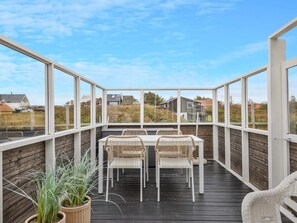 Un espace extérieur abrité, doté d’une table et de chaises, entouré de murs en verre et offrant une vue sur un quartier résidentiel.