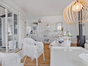 A white-themed room with a large window, a white chair, a white table, and a wood-burning stove. - 5 Star Holiday Home in Lokken (Lokken)