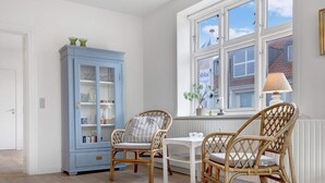 A room with a white door, a blue cabinet with glass doors, two wicker chairs, a small table, and a window with a view of a building. - 5 Star Holiday Home in Lokken (Lokken)
