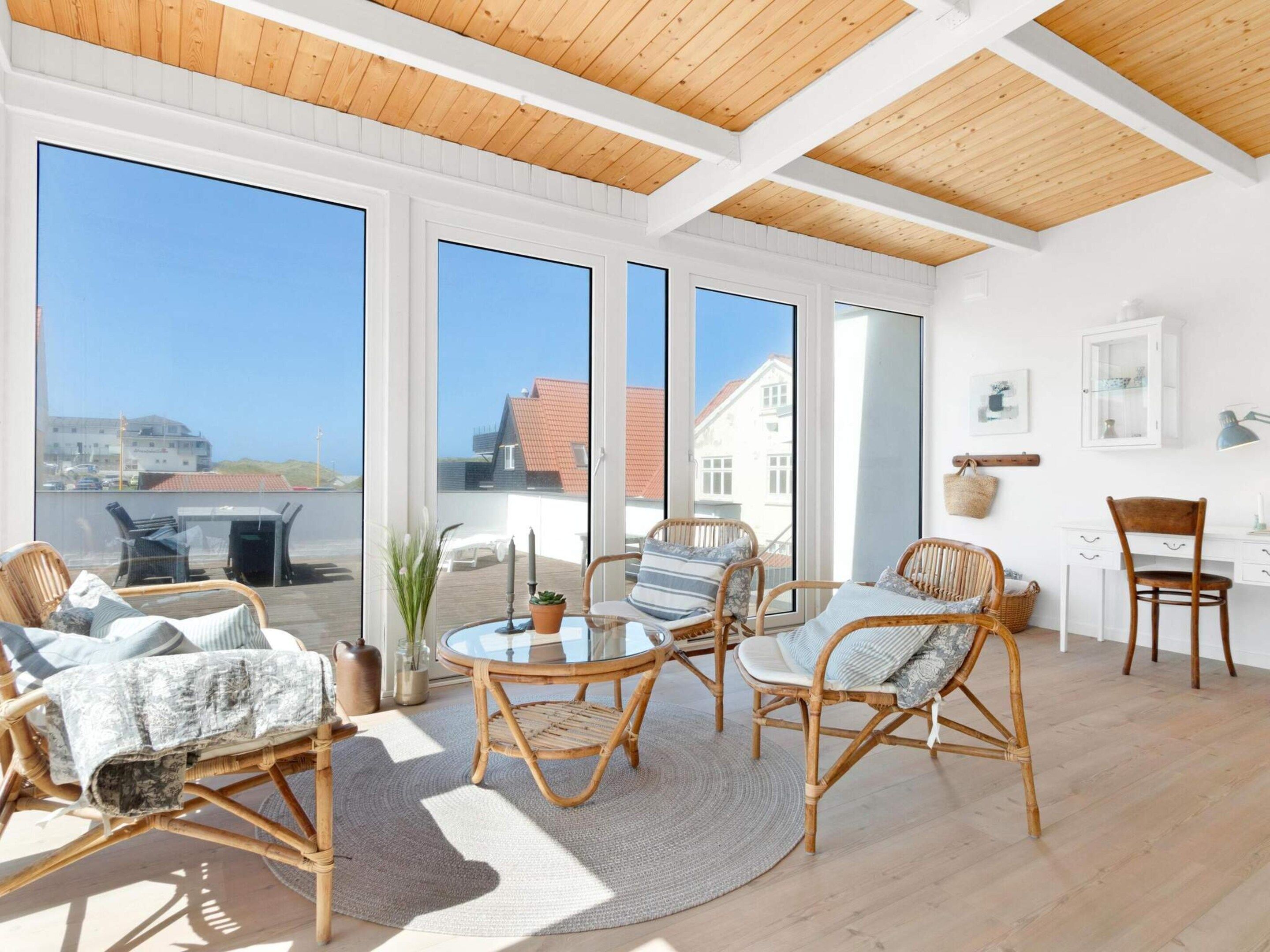 A bright room with large windows, wicker furniture, and a wooden ceiling.